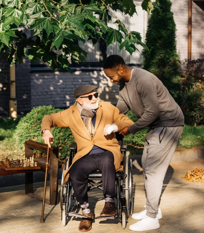 african american man helping senior disabled man to get up from wheelchair on street